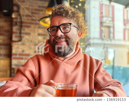 Bearded man in glasses drinking tea at cafe window. Urban lifestyle, contemplation mood, social space, modern city living concept Bearded man in glasses drinking tea at cafe window. Urban lifestyle, contemplation mood, social space, modern city living concept 136919153