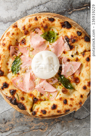Charred pizza with mortadella sausage and burrata cheese close-up on a wooden board. Vertical top view 136919229