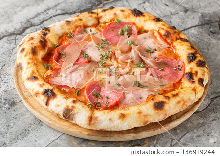 Delicious authentic meat pizza with prosciutto, salami, bacon and ham close-up on a wooden board. Horizontal Delicious authentic meat pizza with prosciutto, salami, bacon and ham close-up on a wooden board. Horizontal 136919244