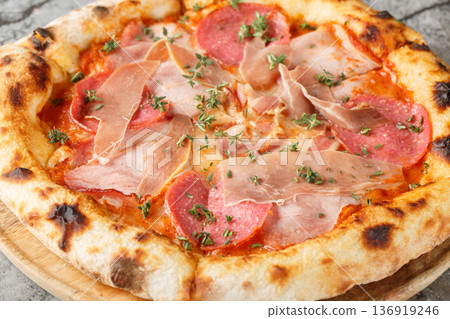 Close-up of neapolitan pizza with prosciutto, salami, tomato sauce and mozzarella on wooden board. Garnished with fresh thyme. Marble background Close-up of neapolitan pizza with prosciutto, salami, tomato sauce and mozzarella on wooden board. Garnished with fresh thyme. Marble background 136919246