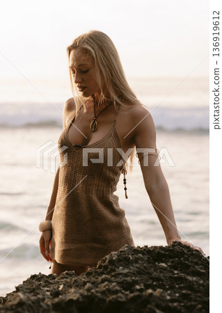 Blonde woman in dress standing on rocks by sea at sunset Blonde woman in dress standing on rocks by sea at sunset 136919612