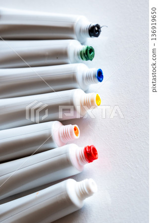 A row of paint tubes in various colors including red, yellow, green, and blue. The tubes are arranged neatly on a white surface, showcasing their vibrant caps. A row of paint tubes in various colors including red, yellow, green, and blue. The tubes are arranged neatly on a white surface, showcasing their vibrant caps. 136919650