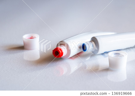 Red and blue tubes of paint on a white surface. The tubes are squeezed slightly, with red and blue caps nearby. Ideal for art and creativity themes. 136919666