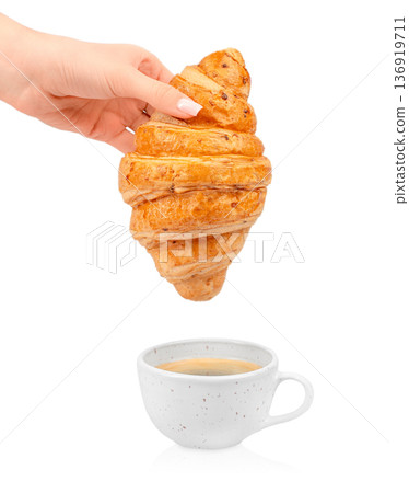 Croissant held above cup of coffee isolated on white background Croissant held above cup of coffee isolated on white background 136919711