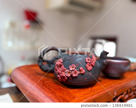 Clay teapot with floral relief on wooden tray indoors. Artisan craftsmanship, tea ceremony culture, handmade pottery, decorative tradition concept Clay teapot with floral relief on wooden tray indoors. Artisan craftsmanship, tea ceremony culture, handmade pottery, decorative tradition concept 136919981