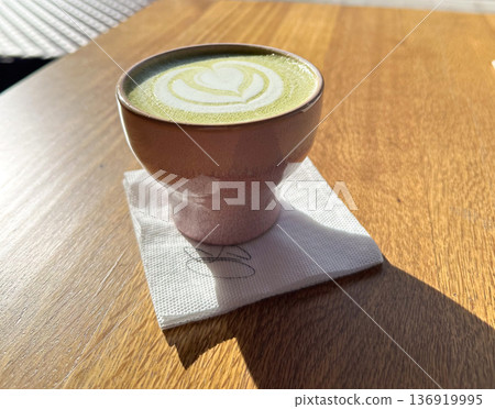 Matcha latte in ceramic cup on wooden table with sunlight. Cafe ritual, mindful pause, wellness lifestyle, slow living morning concept Matcha latte in ceramic cup on wooden table with sunlight. Cafe ritual, mindful pause, wellness lifestyle, slow living morning concept 136919995