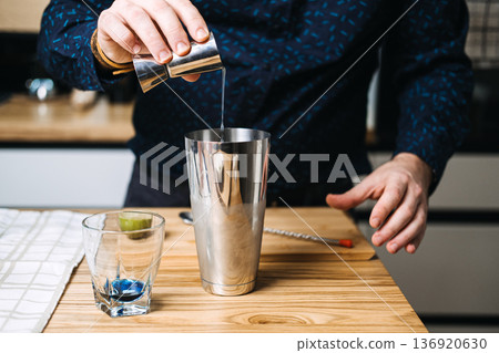 Hand pours citrus juice from metal jigger into stainless steel shaker. Functional beverages, adaptogenic drinks, nootropics, wellness innovation, health-boosting ingredients, botanical infusions. Hand pours citrus juice from metal jigger into stainless steel shaker. Functional beverages, adaptogenic drinks, nootropics, wellness innovation, health-boosting ingredients, botanical infusions. 136920630