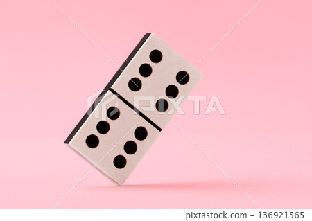 Domino tile stands on its edge against a pink background in a simple display of balance 136921565