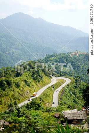 Scenic winding mountain road with vehicles passing through lush green hills Scenic winding mountain road with vehicles passing through lush green hills 136921750