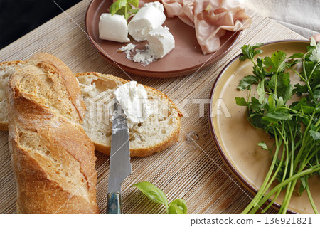 High-quality farm food on wooden cutting board. Top view. Flat lay photo. Soft goat cheese on bread, basil and mortadella sandwich. Italian tradition cuisine. 136921821