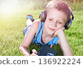 Little boy lying on grass with old audio cassette player 136922224