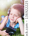 Little boy lying on grass with old audio cassette player 136922225