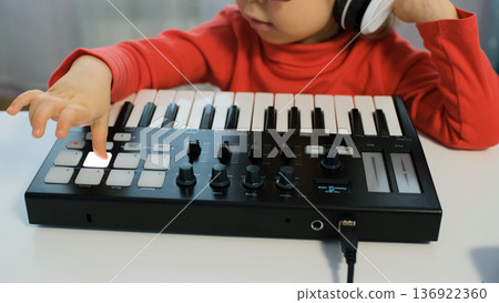 Little girl enjoys music at home on a midi keyboard. She wears headphones and sunglasses while shaking her head and having fun Little girl enjoys music at home on a midi keyboard. She wears headphones and sunglasses while shaking her head and having fun 136922360