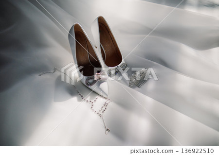 White wedding shoes with jewelry on white fabric White wedding shoes with jewelry on white fabric 136922510