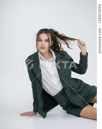 An elegant white woman in business suit talks on a red telephone while sitting on a chair against the backdrop of an isolated space. Office. Curly hair, brown-haired An elegant white woman in business suit talks on a red telephone while sitting on a chair against the backdrop of an isolated space. Office. Curly hair, brown-haired 136922669