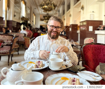 Portrait bearded man enjoying an elegant tea break in a luxurious cafe with classical decor. Luxury restaurant paired with fine tableware and a slice of cake, timeless and refined atmosphere Portrait bearded man enjoying an elegant tea break in a luxurious cafe with classical decor. Luxury restaurant paired with fine tableware and a slice of cake, timeless and refined atmosphere 136922687