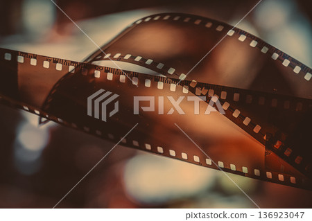 Close up of curved film strip with grunge noise and grain texture glowing in warm light with perforated edges and soft blur. Concept of film nostalgia, cinema memory and analog film art 136923047