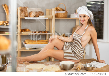 Woman in apron sitting on table in bakery Woman in apron sitting on table in bakery 136924391