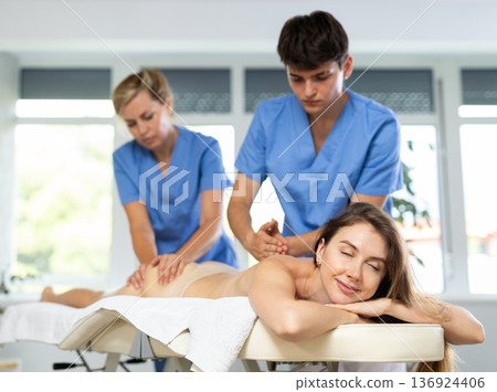 Two unrecognizable female and male masseuses perform stroking and rubbing of muscle of back to girl Two unrecognizable female and male masseuses perform stroking and rubbing of muscle of back to girl 136924406