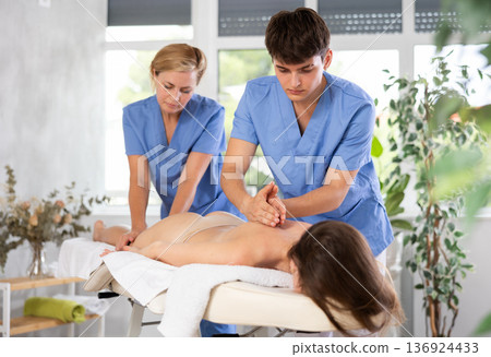 Professional masseur and masseuse performing back massage for female patient Professional masseur and masseuse performing back massage for female patient 136924433