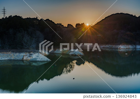 Early spring 2026: The sun sets behind the mountains on the opposite bank of Nunome Dam, where water levels remain low. Early spring 2026: The sun sets behind the mountains on the opposite bank of Nunome Dam, where water levels remain low. 136924843