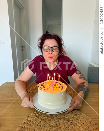 Woman blowing out candles on birthday cake. Celebration, tradition and joyful wish-making moment at festive party. Woman blowing out candles on birthday cake. Celebration, tradition and joyful wish-making moment at festive party. 136924884