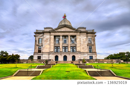 Arkansas State Capitol building in Little Rock. Historic Neoclassical government architecture features a limestone facade and dome under a blue sky with clouds 136925019