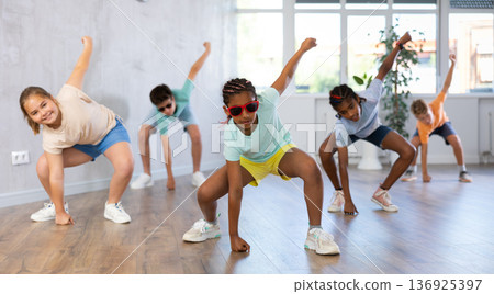 Positive juvenile girl engaged in Breakdancing in training room with children's group 136925397