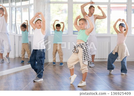 Young girl and group of positive children practicing energetic hip hop movements at dance school Young girl and group of positive children practicing energetic hip hop movements at dance school 136925409