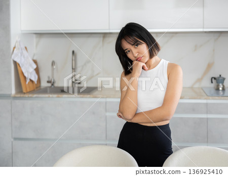 Sad young Asian girl standing at table in the kitchen 136925410