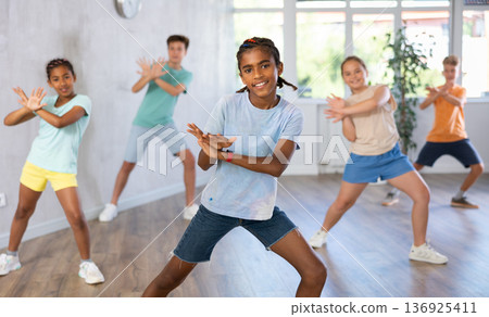 Positive juvenile boy engaged in Breakdancing in training room with children's group 136925411