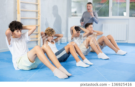Underage boy practicing press in lying position with other attendees and trainer 136925416