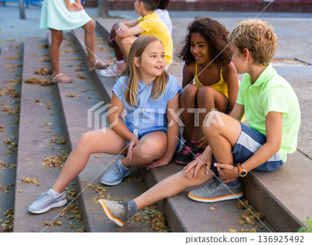 Positive tweenagers friendly blabbing while sitting on steps outdoors Positive tweenagers friendly blabbing while sitting on steps outdoors 136925492