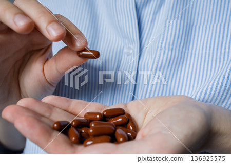 Woman talking one brown vitamin pill from handful of tablets. Vitamins for hair growth and improvement of skin and nails condition. Dietary supplements complex for health improvement. 136925575