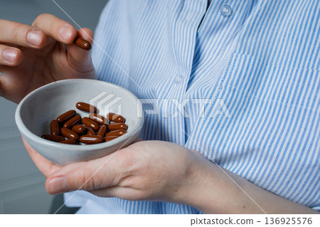 Small bowl with brown vitamin capsules in woman hands close up. Dietary supplements, biohacking, home treatment. Small bowl with brown vitamin capsules in woman hands close up. Dietary supplements, biohacking, home treatment. 136925576