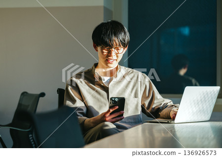 A young man looking at his smartphone in the office in the evening 136926573