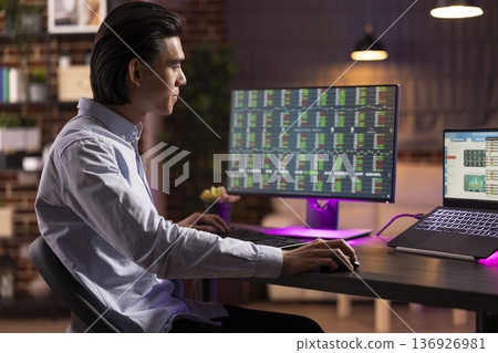 Male business consultant analyzing trading analysis and investment data from home office. Young entrepreneur working remotely, focusing on stock market and financial statistics of startup company. Male business consultant analyzing trading analysis and investment data from home office. Young entrepreneur working remotely, focusing on stock market and financial statistics of startup company. 136926981