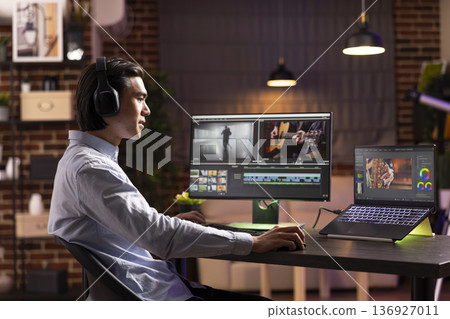 Young man focused on syncing recorded audio and video during post film production. Self employed videographer listening to music on headphones for enjoyable editing workflow on digital devices at home 136927011