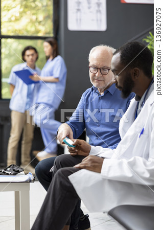 African american medic checks blood sugar levels during medical examination using glucometer. Clinical assessment takes place in waiting area, ensuring accurate diabetes screening and patient care. African american medic checks blood sugar levels during medical examination using glucometer. Clinical assessment takes place in waiting area, ensuring accurate diabetes screening and patient care. 136927075