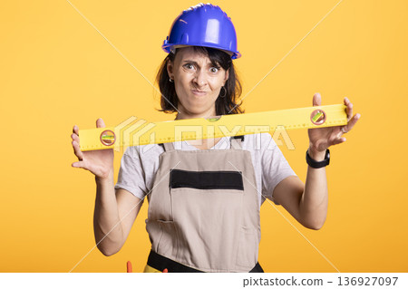 Female builder grips measuring level, questioning accuracy of measurement. Woman contractor angrily holds construction tool, representing frustration in DIY adjustments and onsite evaluation. Female builder grips measuring level, questioning accuracy of measurement. Woman contractor angrily holds construction tool, representing frustration in DIY adjustments and onsite evaluation. 136927097