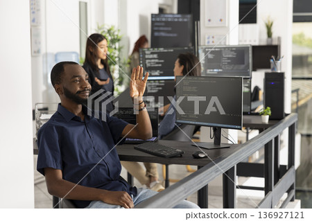 Black male software engineer interacts with invisible holographic interface, using hand gestures to explore augmented reality and futuristic digital workspace in a modern tech office. Black male software engineer interacts with invisible holographic interface, using hand gestures to explore augmented reality and futuristic digital workspace in a modern tech office. 136927121