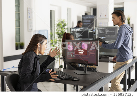 Asian female technology professional reacts to bad news on device screen, signaling computer crash, virus infection, or network error during office work in a high pressure IT environment. 136927123