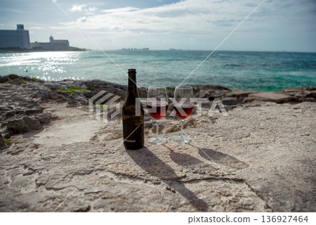 Two wine glasses and bottle on coastline with ocean and resort in background 136927464