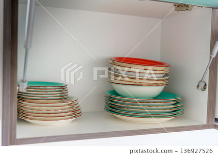 Organized kitchen cabinet with colorful stacked dishes and bowls Organized kitchen cabinet with colorful stacked dishes and bowls 136927526