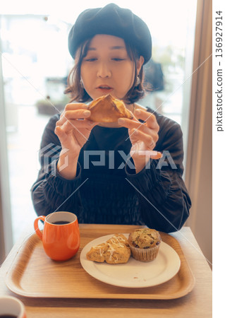 Japanese woman eating bread at a cafe 136927914