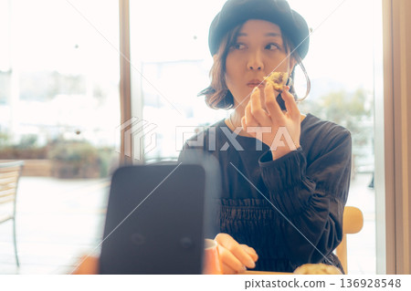 A woman eating bread through her smartphone at a cafe A woman eating bread through her smartphone at a cafe 136928548