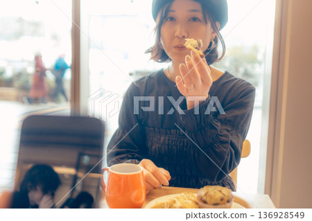 一位女士在咖啡館一邊用智慧型手機看麵包一邊吃東西。 136928549