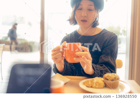 A woman eating bread through her smartphone at a cafe 136928550