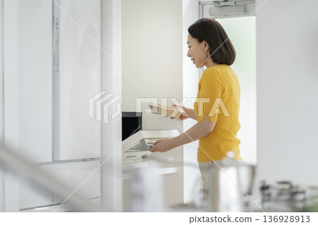 Middle-aged woman heating lunch in the microwave Middle-aged woman heating lunch in the microwave 136928913
