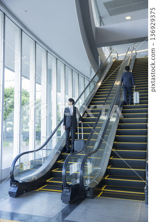 Businessman riding escalator Businessman riding escalator 136929375